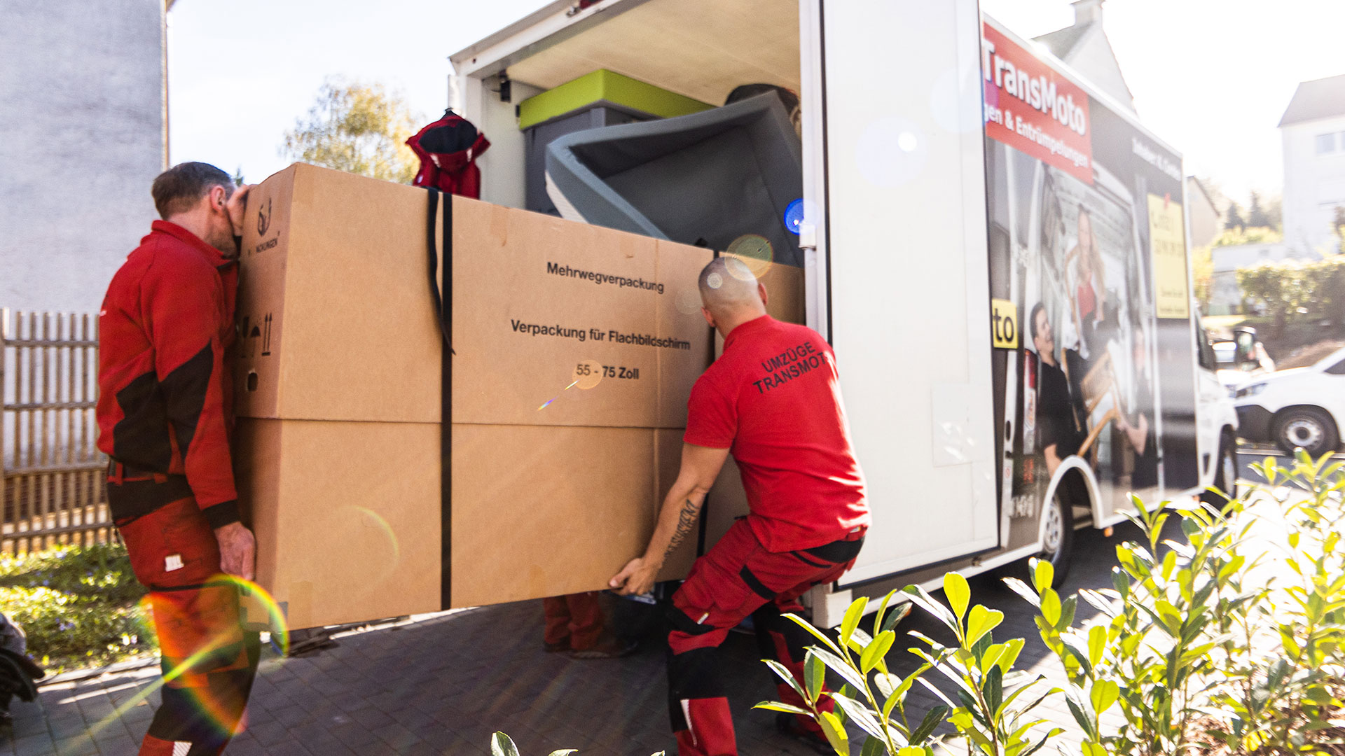 Zwei Möbelpacker laden großen Karton in Umzugswagen