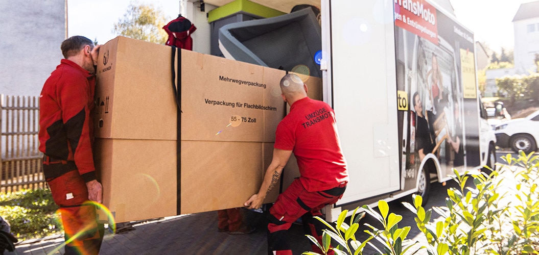 Zwei Möbelpacker laden großen Karton in Umzugswagen
